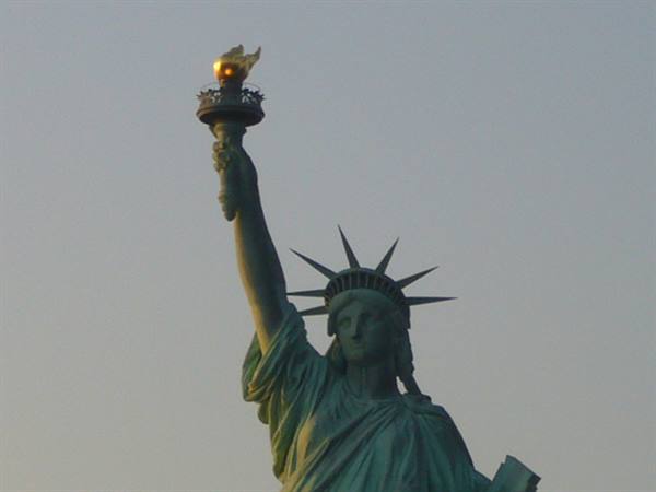 The Statue of Liberty raising her golden torch against the evening sky