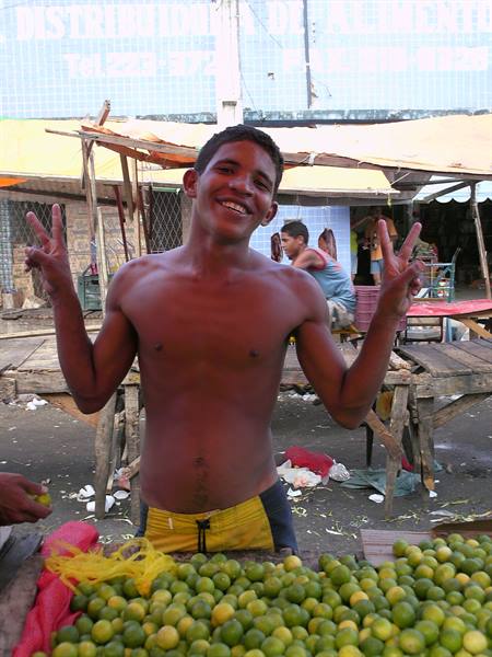 Smiling young man flashing peace signs at market stall of green limes