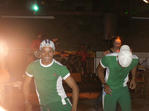 Dancers in green and white outfits perform in front of a live band