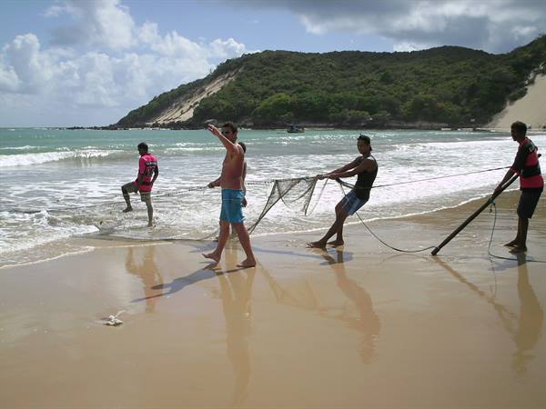 Fishermen pulling a fishing net on wet sand, green hill behind
