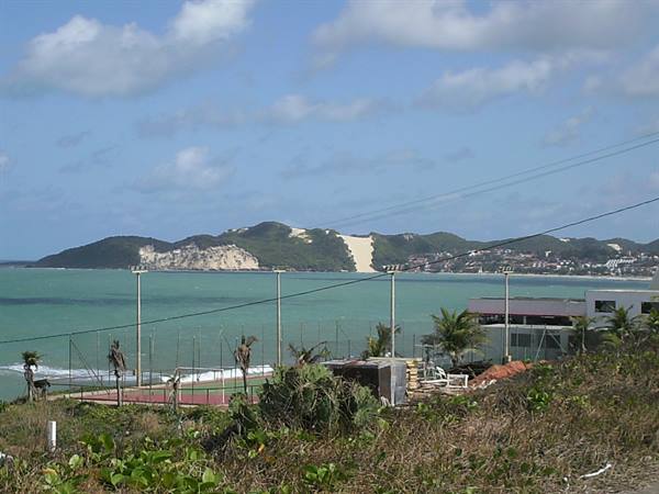 Beach with sand dunes, tennis courts and green vegetation, turquoise bay