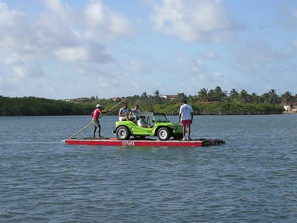 Ferry raft crossing the river carrying a green dune buggy