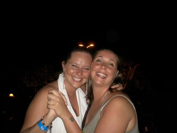 Two smiling friends embrace at night, lit by camera flash