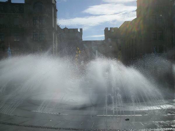 Water jets from a fountain in front of old stone buildings
