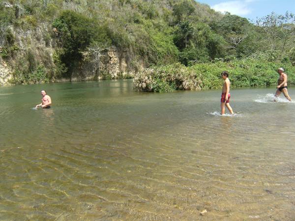 Bathers wading in a green river with sandy shore and wooded hill
