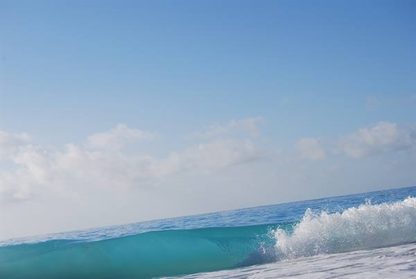 Turquoise wave breaking on the beach under blue sky