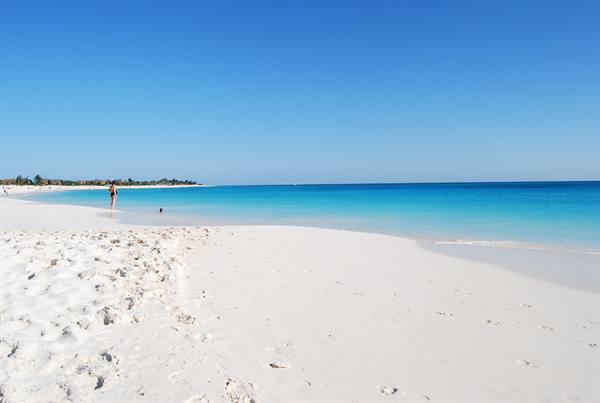 White sand beach, person swimming in turquoise water under blue sky