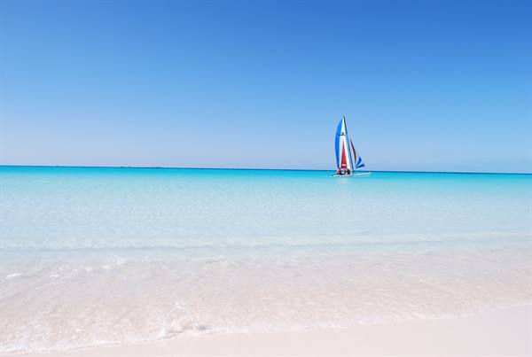 White sand beach, turquoise water, sailboat on the horizon line