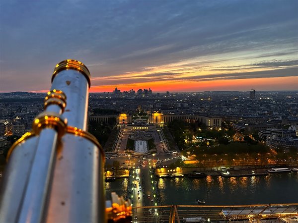 Golden telescope atop the Eiffel Tower overlooking lit Trocadéro at dusk