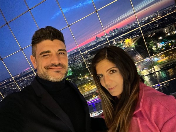 Couple taking a selfie behind the glass wall overlooking Paris at dusk