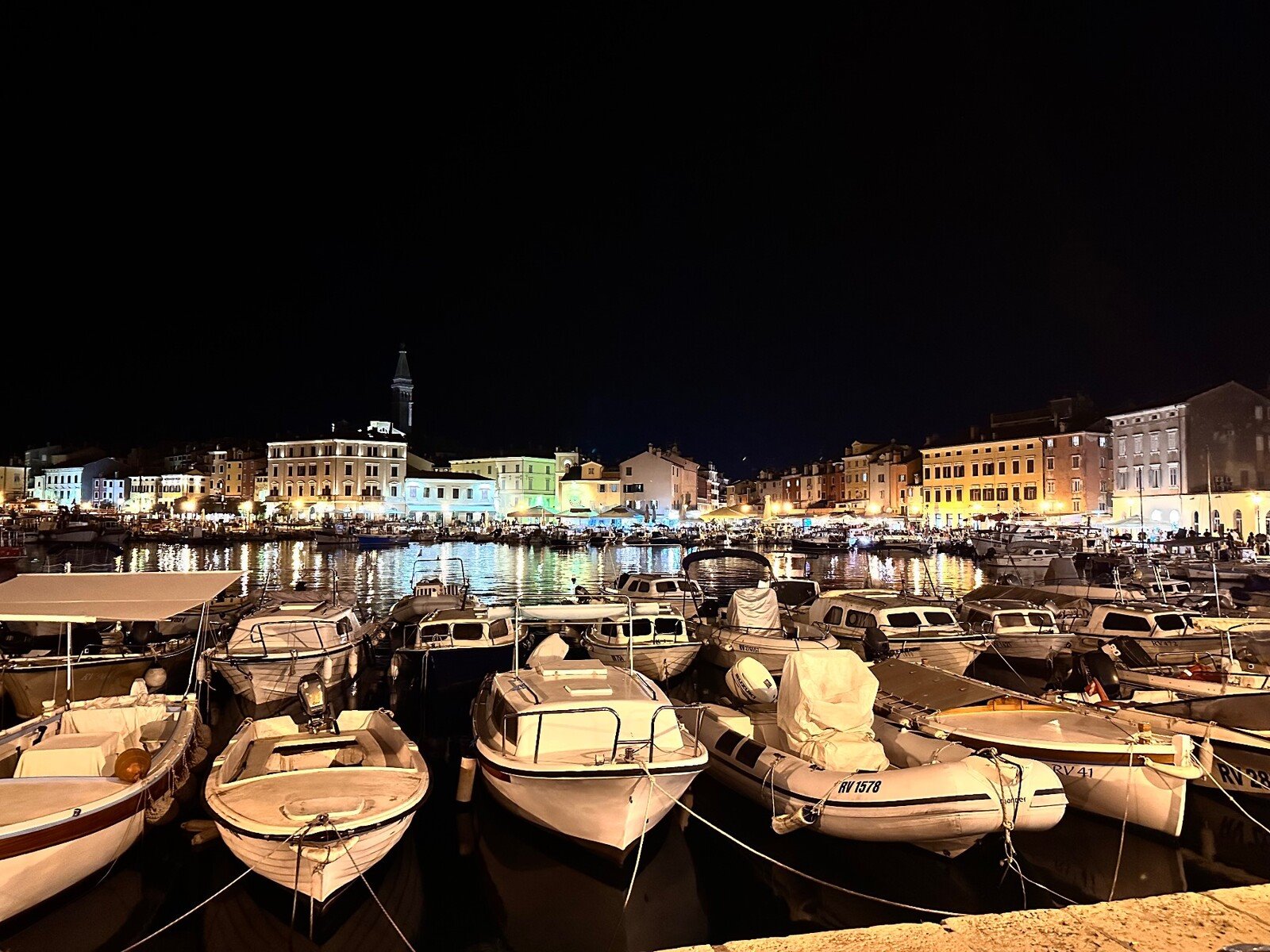 Il porto di Rovigno di notte: luci danzanti sull'acqua e barche addormentate.