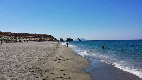 A silent walk on Vlychada beach, among dark sand and waves.