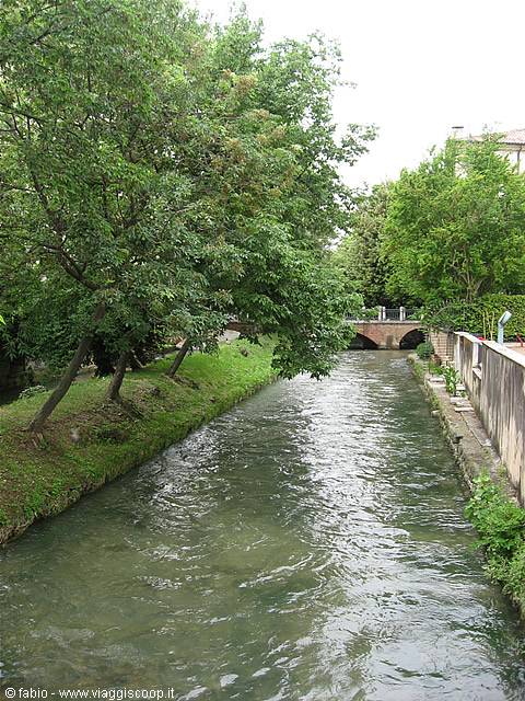 tree-lined canal with small brick bridge and slow green water