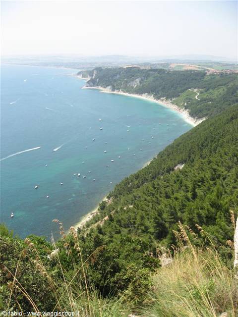 Turquoise bay with boats, white beach and pine forest on Monte Conero