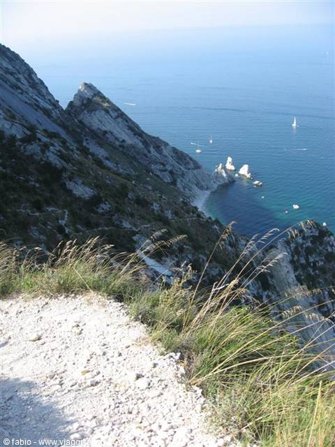 Gravel trail on Monte Conero, limestone cliffs above blue sea with sailboats