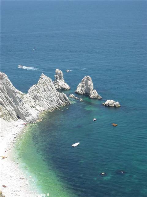White rocks plunging into turquoise sea, anchored boats and pebble beach