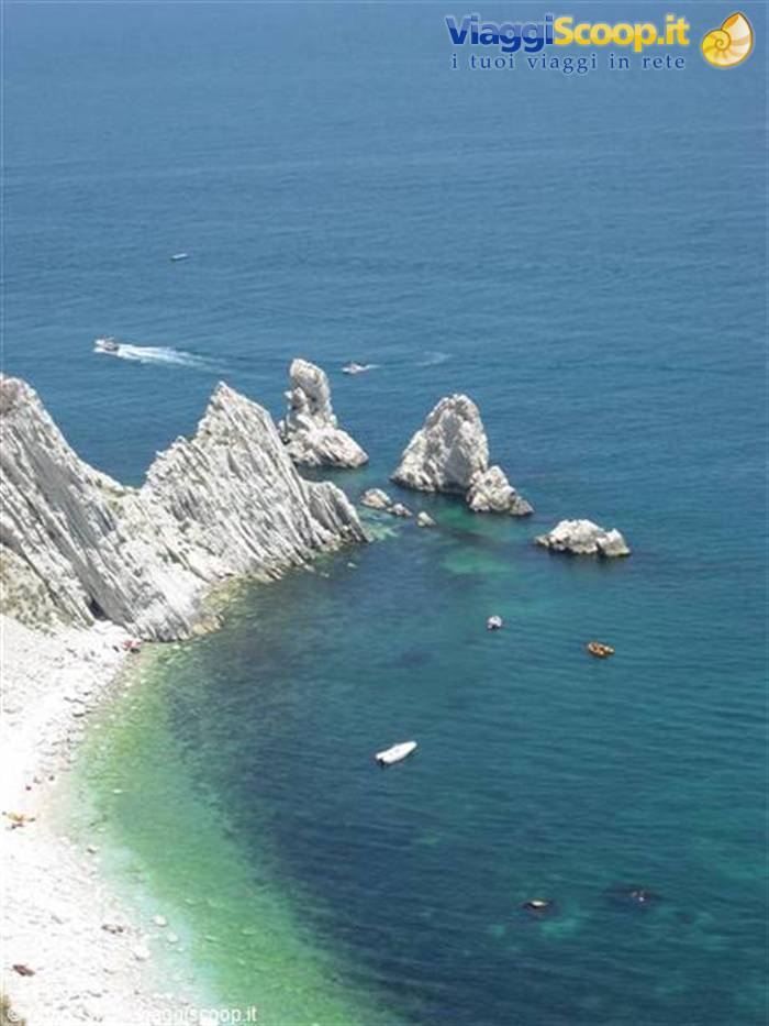 White rocks plunging into turquoise sea, anchored boats and pebble beach