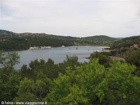 bay with moored boats among green hills and Mediterranean scrub, cloudy sky
