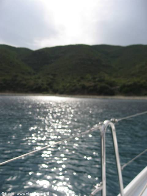 From the sailboat, steel pulpit rail over sparkling sea facing green hills