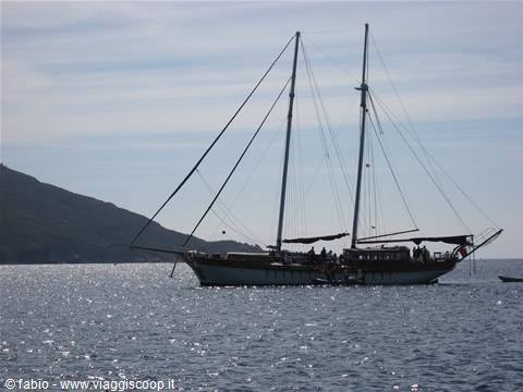 Sailing schooner anchored on sparkling sea in front of the hill