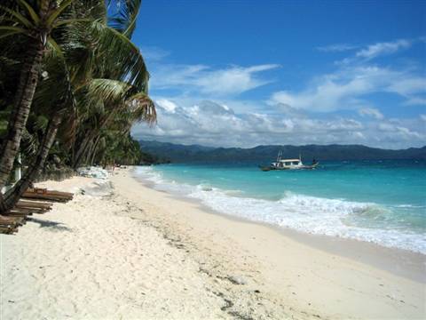 Traditional bangka boat anchored off White Beach, Boracay, among palms and turquoise waves