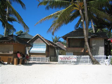 Thatched huts and palm trees on white sand, Mabuhay sign, blue sky