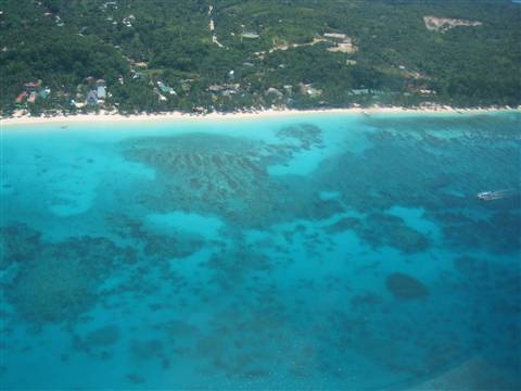 White beach seen from the air, turquoise coral reef and boats