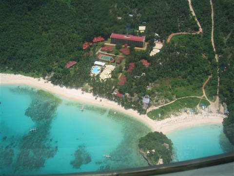 White sand tropical beach with turquoise water seen from plane, resort with pool among palms
