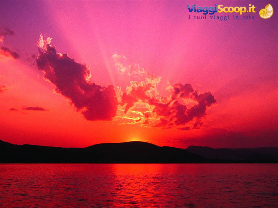 Sun sinking behind a dark hill, vivid pink sky reflecting red over the sea