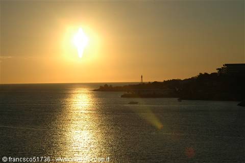 Low sun over the sea with golden reflections, silhouetted coast with buildings and lighthouse