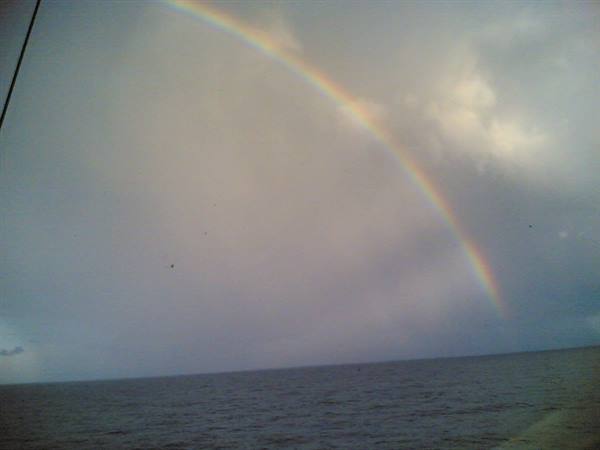 Rainbow over gray sea from a boat, cloudy sky