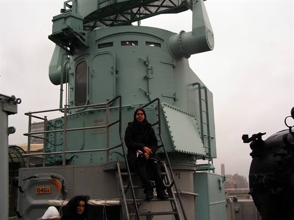 Woman sitting on metal ladder beside anti-aircraft turret aboard the Intrepid, New York