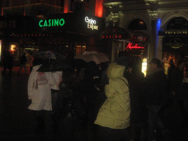 People with umbrellas under the Casino Empire neon sign, Leicester Square