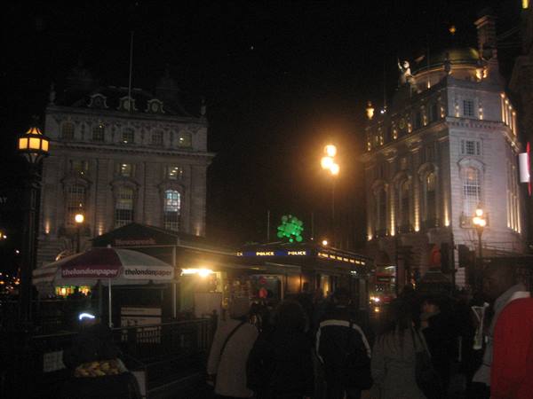 Piccadilly Circus at night, lit buildings, crowd and kiosk with umbrellas