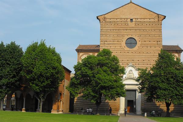 Brick facade of Santo Stefano basilica in Bologna framed by green trees