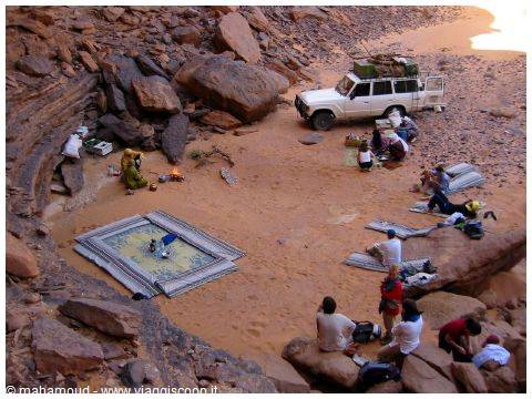 Bedouin camp on red sand: white 4x4, carpets and travelers seated among rocks