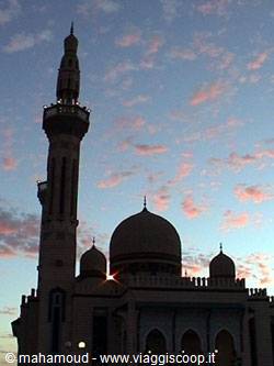 Minaret and domes of a mosque silhouetted at dusk with pink clouds