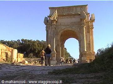 Tourists walk under the Arch of Septimius Severus at Leptis Magna in sunlight