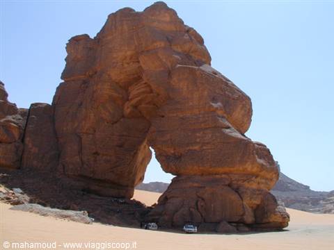 Natural sandstone rock arch in the desert, 4x4 vehicles parked below