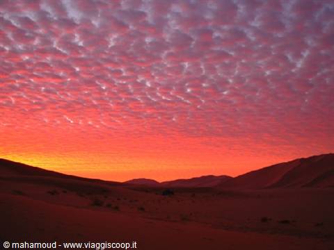 Sand dunes beneath a red mottled cloudy sky at dusk