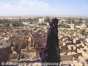Man in indigo turban standing over earthen mud-brick rooftops