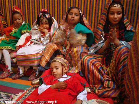 Berber children in colorful traditional dresses with silver jewelry, inside a tent