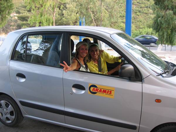 Two smiling women in the grey rental car, one waving from the window