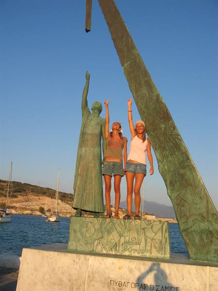 Two tourists pose beneath the bronze Pythagoras statue on Samos harbor