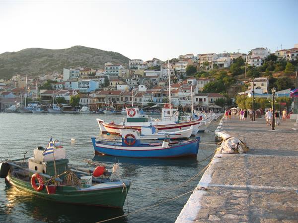 Fishing boats moored at Pythagoreio harbor, colorful houses on the hillside