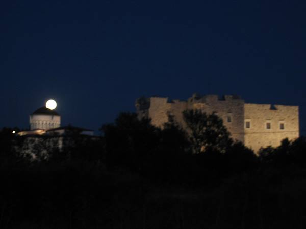 Full moon above a domed church and a floodlit stone castle at night