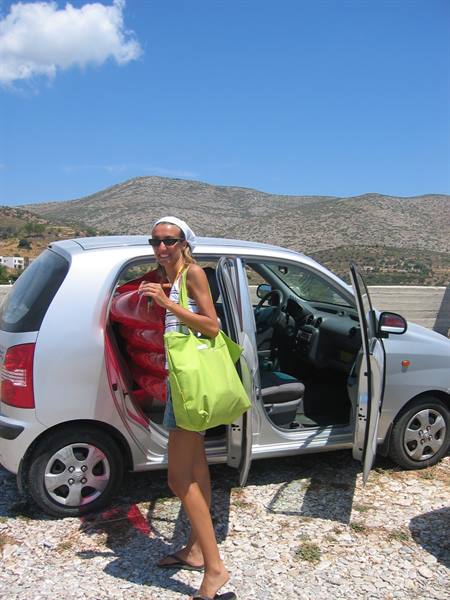 Girl with green bag beside an open silver car, arid hills behind