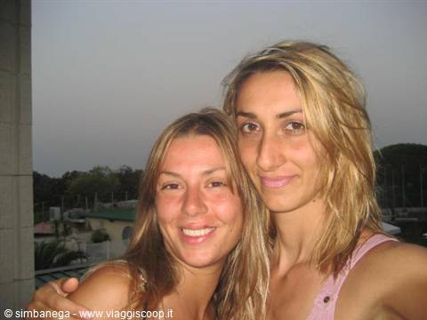 Two smiling blonde women hugging in an evening selfie on a balcony