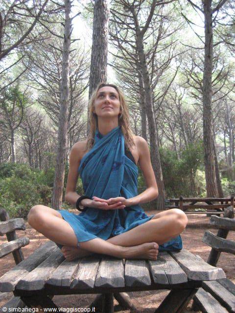 Woman meditating cross-legged on wooden table in sunny pine forest