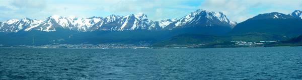 Snow-capped mountain range above blue sea, small town along the shore